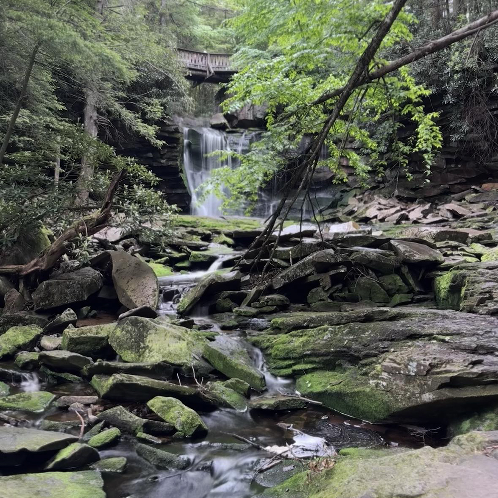 Distant view of the base of Elakala Falls with large rocks scattered around, showing the rocky approach to get closer to the waterfall.