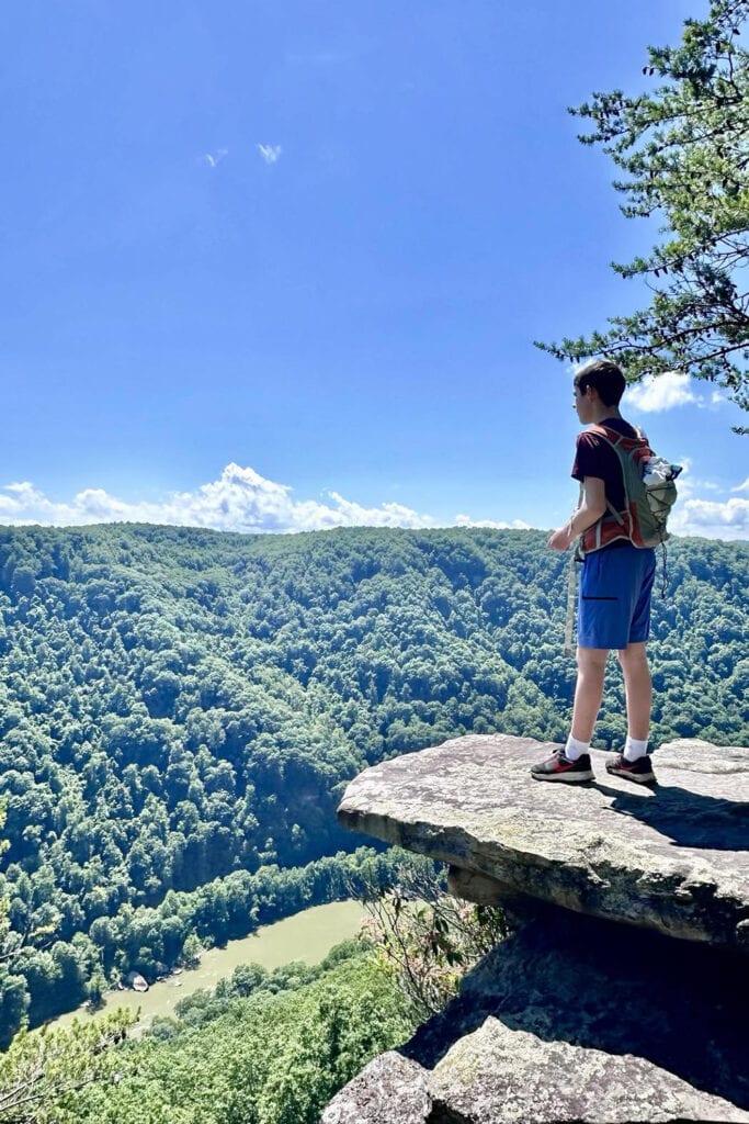 Boy standing on a rock that over hangs the New River Gorge. He's taking in the view of the New River